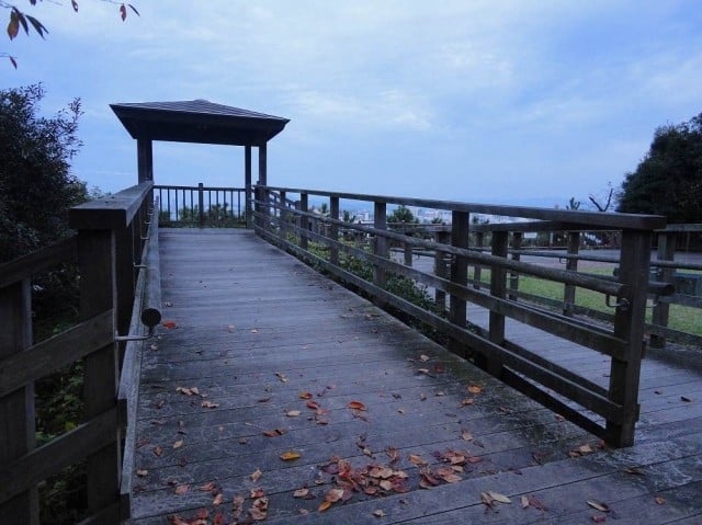 手前中央から奥へ向かって緩やかな傾斜の木製デッキのスロープがあり、デッキ板には落ち葉が散らばっている。左右に手すり付きのデッキが延び、スロープの先には四本の柱と屋根からなるあずまやが設置されている。